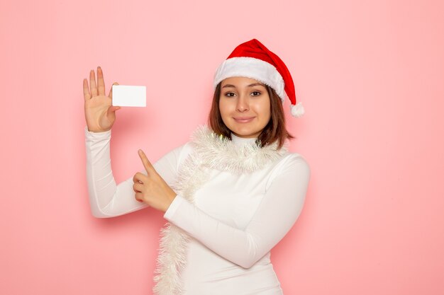 Vista frontal joven mujer sosteniendo tarjeta bancaria blanca sobre pared rosa Navidad año nuevo moda color dinero vacaciones