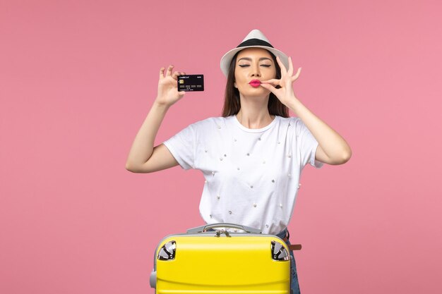 Vista frontal joven mujer sosteniendo una tarjeta bancaria negra en el viaje de color rosa claro viaje de escritorio
