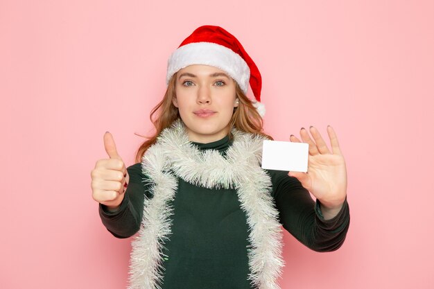 Vista frontal joven mujer sosteniendo una tarjeta bancaria en la pared rosa modelo de color vacaciones navidad año nuevo emoción