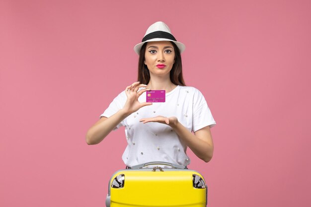 Vista frontal joven mujer sosteniendo tarjeta bancaria en pared rosa viaje mujer vacaciones dinero