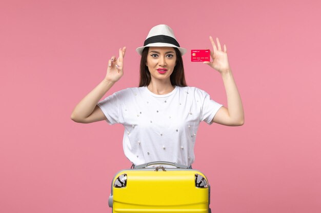 Vista frontal joven mujer sosteniendo una tarjeta bancaria roja en el escritorio rosa viaje color viaje verano