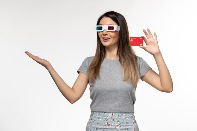 Vista frontal joven mujer sosteniendo tarjeta bancaria roja en gafas de sol d en escritorio blanco