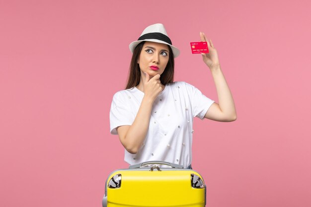 Vista frontal joven mujer sosteniendo una tarjeta bancaria roja en la pared rosa color viaje viaje de verano