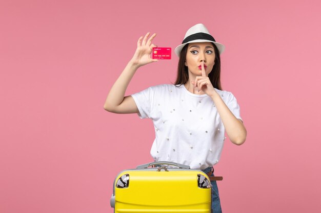 Vista frontal joven mujer sosteniendo una tarjeta bancaria roja en la pared rosa color de viaje de viaje de verano