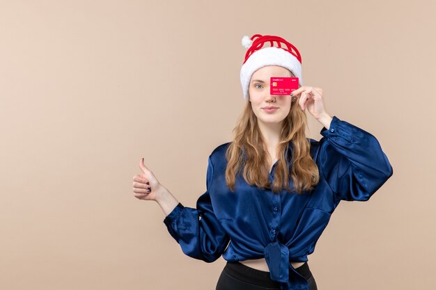 Vista frontal joven mujer sosteniendo tarjeta bancaria roja sobre fondo rosa vacaciones de año nuevo foto de navidad emoción dinero