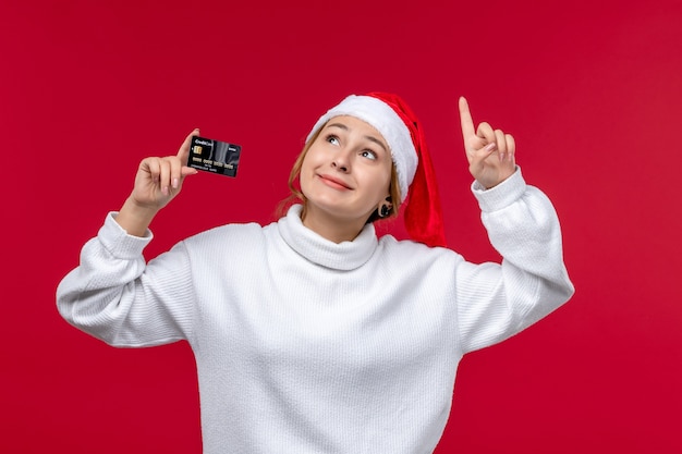 Vista frontal joven mujer sosteniendo tarjeta bancaria sobre fondo rojo claro
