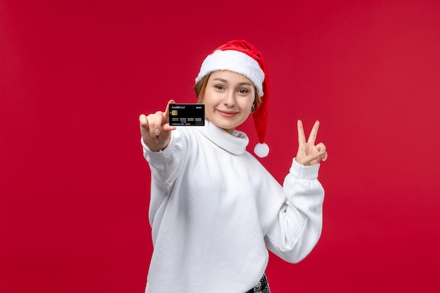 Vista frontal joven mujer sosteniendo tarjeta bancaria sobre fondo rojo.