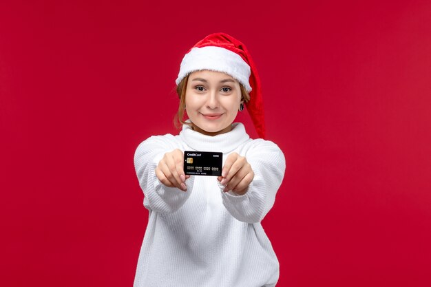 Vista frontal joven mujer sosteniendo tarjeta bancaria sobre fondo rojo.