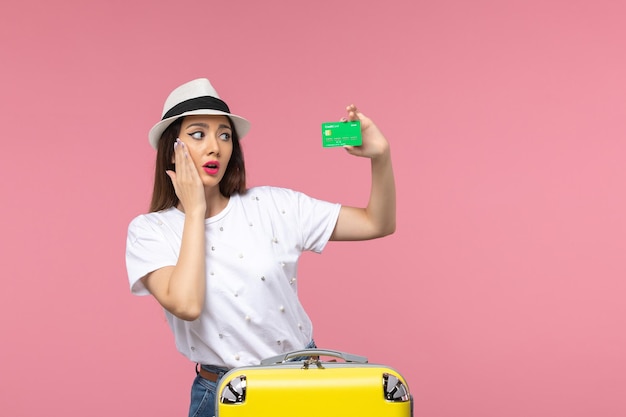 Vista frontal joven mujer sosteniendo tarjeta bancaria verde en la pared rosa emoción mujer viaje verano