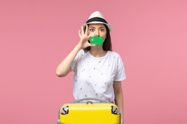 Vista frontal joven mujer sosteniendo tarjeta bancaria verde en la pared rosa emociones viaje de mujer de verano