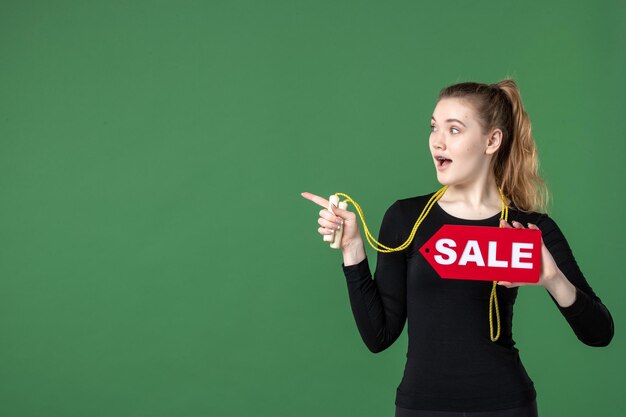 Vista frontal joven mujer sosteniendo venta escrito sobre fondo verde color de cuerpo salud mujer deporte gimnasia entrenamiento compras atleta