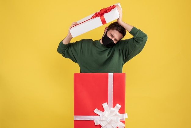 Vista frontal joven con los ojos cerrados de pie detrás de gran caja de regalo en amarillo