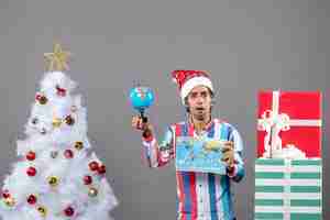 Foto gratuita vista frontal joven con ojos curiosos sosteniendo un mapa del mundo y un globo alrededor del árbol de navidad y regalos