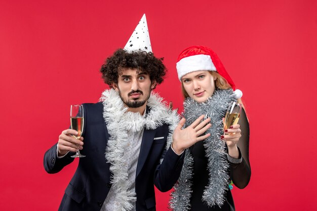 Vista frontal de la joven pareja celebrando el año nuevo en la pared roja vacaciones navidad color amor