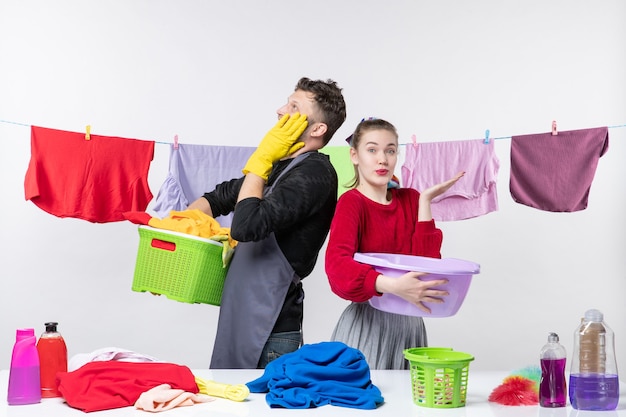 Vista frontal de la joven pareja preparando lavar la ropa en la pared blanca