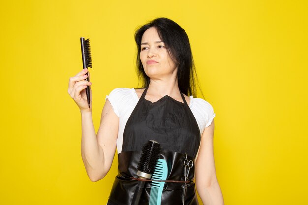 Una vista frontal joven peluquera en camiseta blanca capa negra con cepillo negro onda pelo disgustado