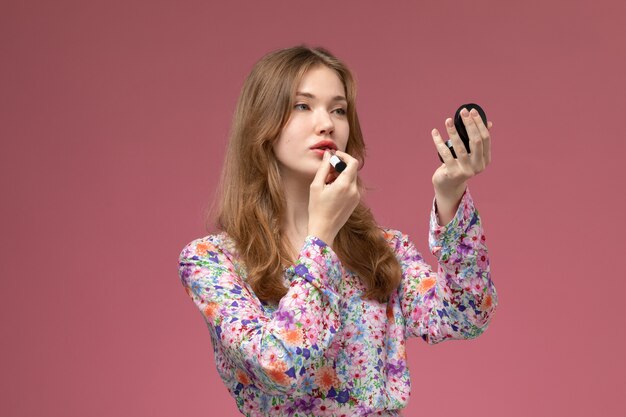 Vista frontal joven pintando sus labios con lápiz labial rosa