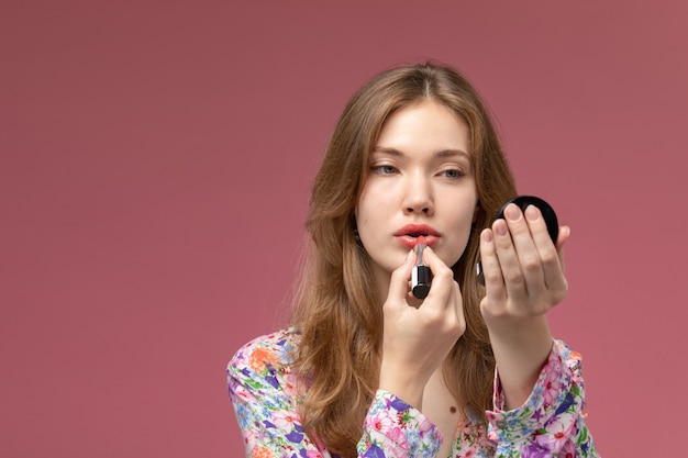 Vista frontal joven pintando sus labios con lápiz labial y usando mini espejo