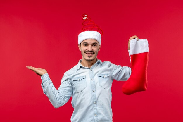 Vista frontal del joven posando con calcetín de Navidad en la pared roja