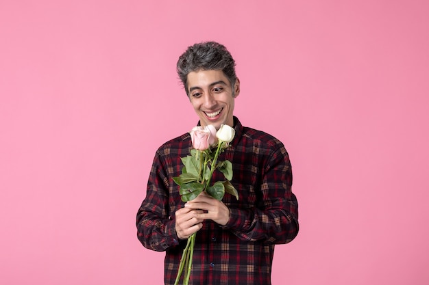 Vista frontal joven posando con hermosas rosas rosadas en la pared rosa