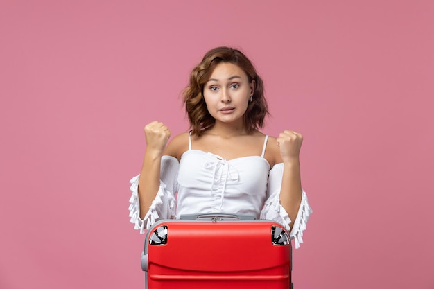 Vista frontal de la joven preparándose para las vacaciones con su bolso rojo en la pared de color rosa claro