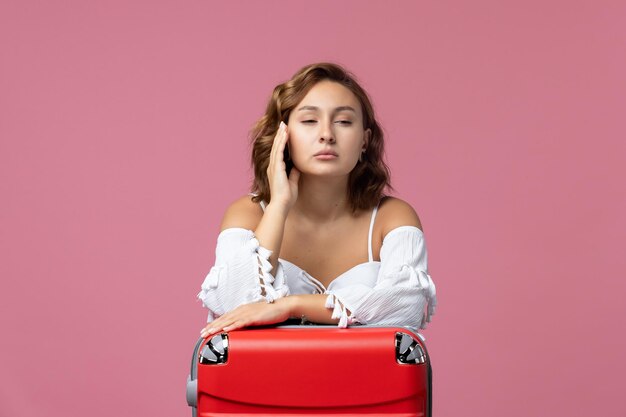 Vista frontal de la joven preparándose para las vacaciones con su bolso rojo en la pared rosa