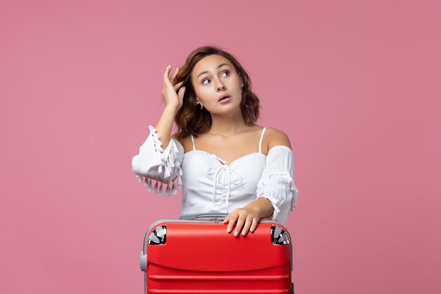 Vista frontal de la joven preparándose para el viaje con bolsa roja en la pared rosa