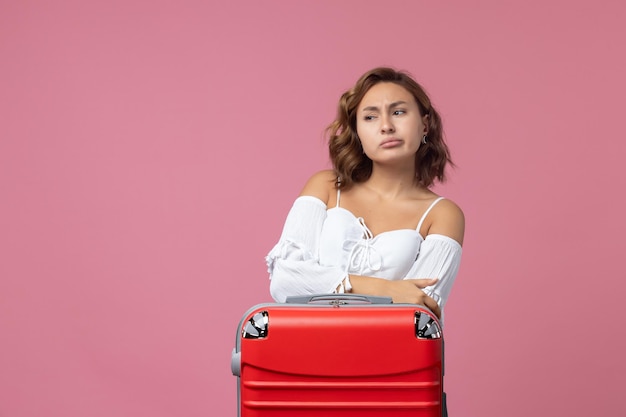 Vista frontal de la joven preparándose para el viaje con bolsa roja en la pared rosa