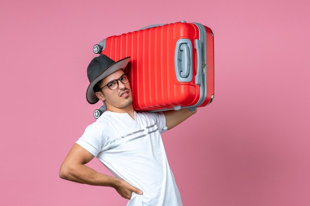 Vista frontal del joven que va de vacaciones y que sostiene la bolsa roja en la pared rosa