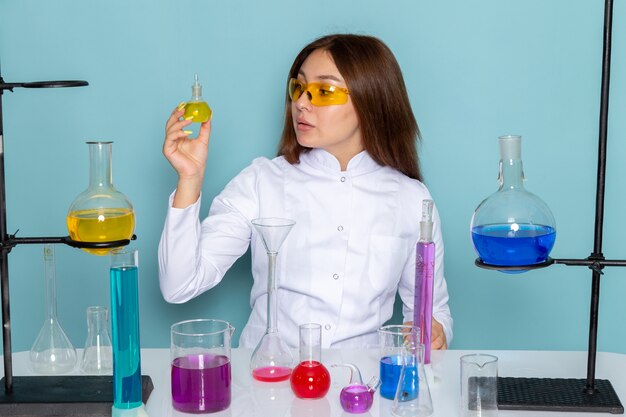 Vista frontal del joven químico Feman en traje blanco delante de la mesa trabajando con soluciones