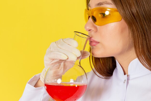 Vista frontal del joven químico femenino en traje blanco con solución química