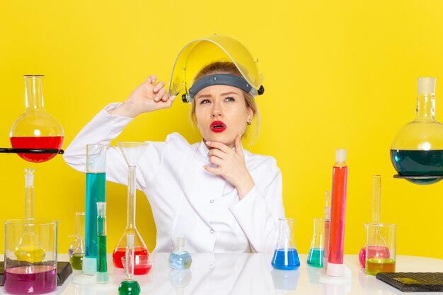 Vista frontal joven químico femenino en traje blanco con soluciones ed pensando en el espacio amarillo ciencia química s