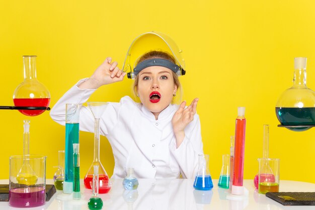 Vista frontal joven químico femenino en traje blanco con soluciones ed quitándose el casco en el trabajo de química espacial amarillo