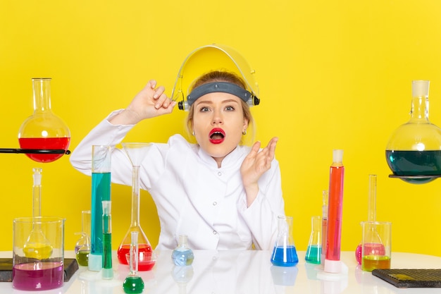 Vista frontal joven químico femenino en traje blanco con soluciones ed quitándose el casco en el trabajo de química espacial amarillo