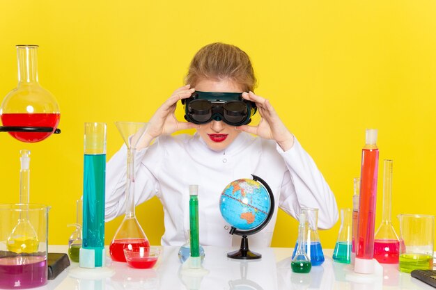 Foto gratuita vista frontal joven químico femenino en traje blanco con soluciones ed trabajando con ellos con máscara en la ciencia química espacial amarilla