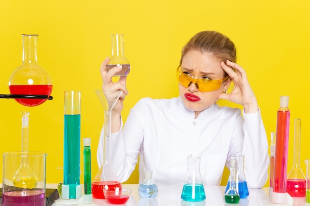 Foto gratuita vista frontal joven químico femenino en traje blanco con soluciones ed trabajando con ellos sentado en la ciencia química espacial amarilla