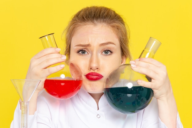 Foto gratuita vista frontal joven químico femenino en traje blanco sosteniendo diferentes soluciones en el trabajo de química espacial amarillo