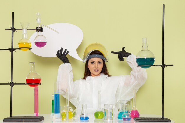 Vista frontal joven químico femenino en traje de protección especial con cartel blanco en la pared verde trabajo laboratorio químico química ciencia femenina