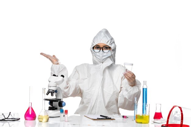 Vista frontal joven químico femenino en traje de protección especial con matraz vacío sobre fondo blanco laboratorio covid- salud del virus de la química