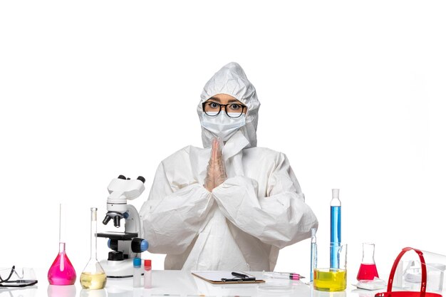 Vista frontal joven químico femenino en traje de protección especial orando sobre fondo blanco laboratorio de virus covid- química