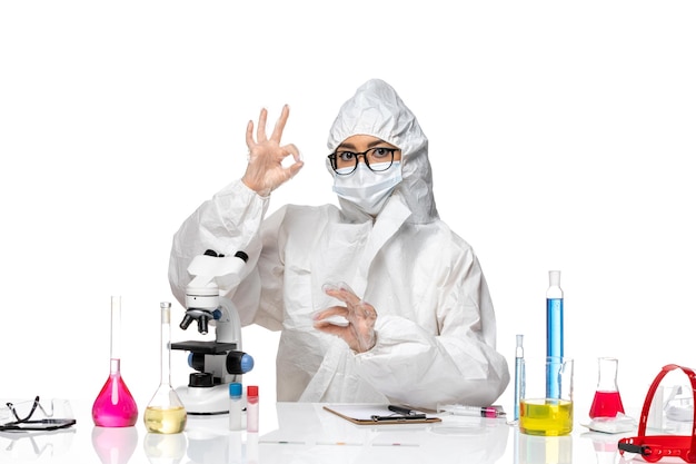 Vista frontal joven químico femenino en traje de protección especial que trabaja con microscopio en el laboratorio de virus de escritorio blanco covid- química de la salud