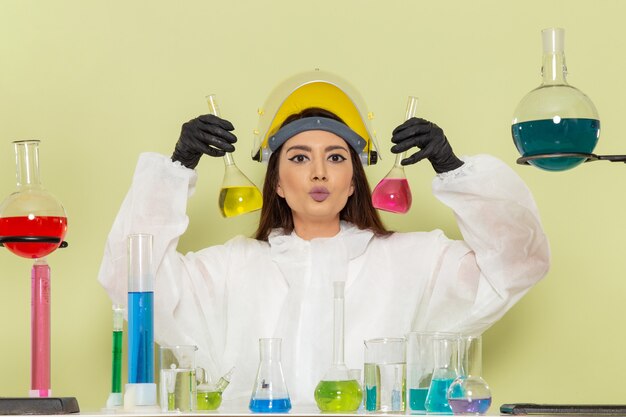 Vista frontal joven químico femenino en traje de protección especial que trabaja con soluciones en el escritorio verde laboratorio químico trabajo de química ciencia femenina