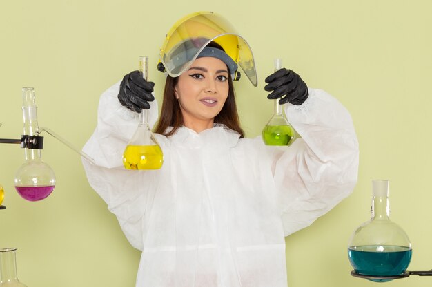 Vista frontal joven químico femenino en traje de protección especial sosteniendo soluciones coloreadas en la pared verde química química trabajo laboratorio de ciencias femenino