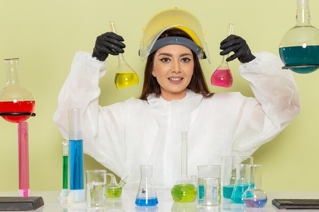 Vista frontal joven químico femenino en traje de protección especial trabajando con soluciones en el escritorio verde química química trabajo laboratorio de ciencias femenino