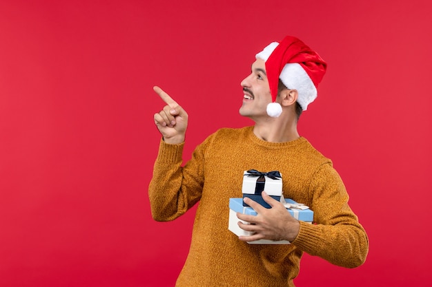 Vista frontal del joven con regalos de año nuevo en la pared roja