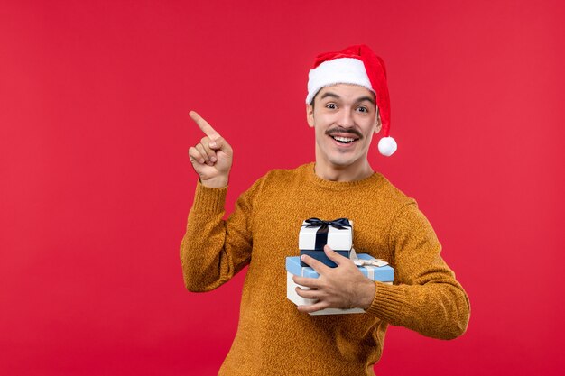 Vista frontal del joven con regalos de año nuevo en la pared roja