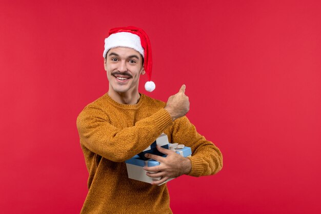 Vista frontal del joven con regalos de año nuevo en la pared roja