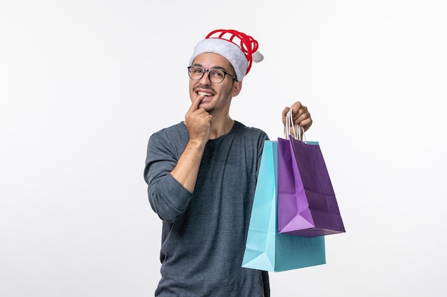 Vista frontal del joven con regalos después de comprar en la pared blanca