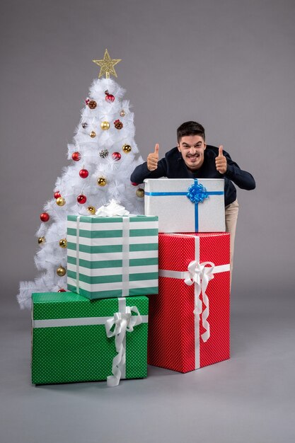 Vista frontal joven con regalos de Navidad en el gris