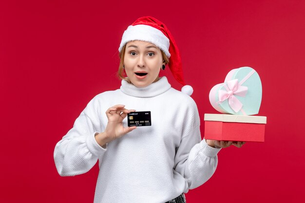 Vista frontal joven con regalos y tarjeta bancaria en el escritorio rojo